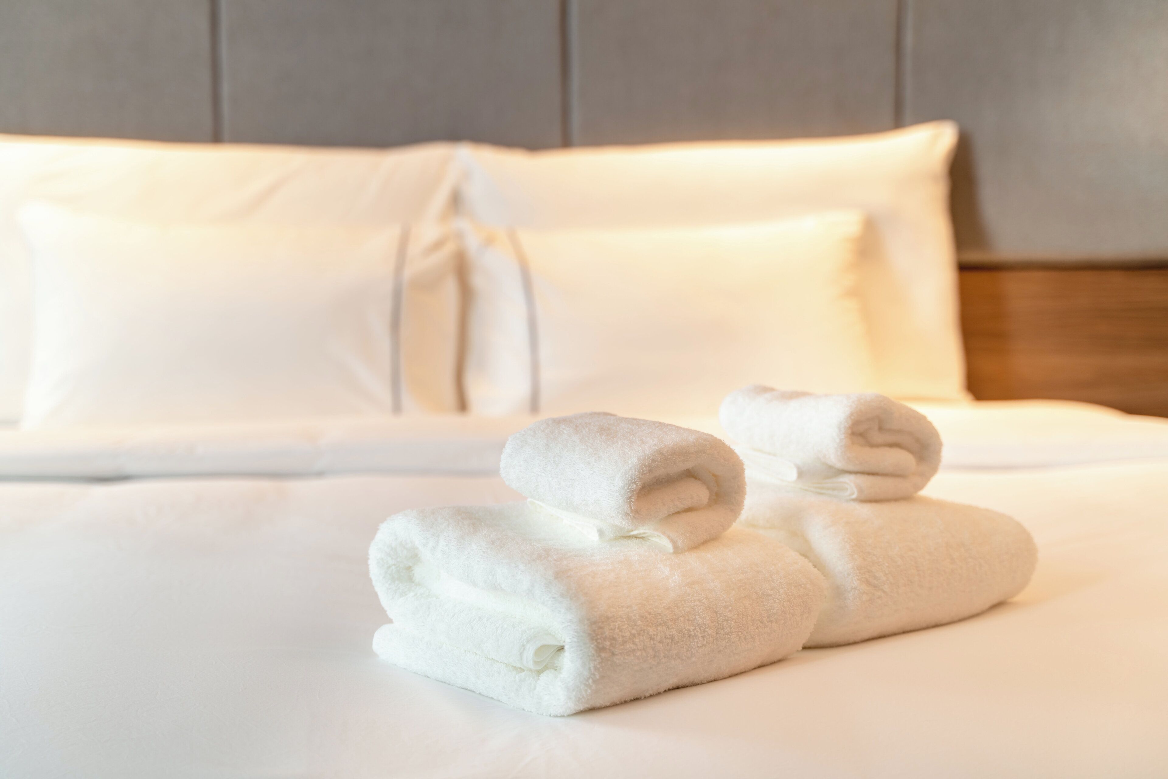 Una cama bien hecha con sábanas blancas y dos toallas enrolladas encima.