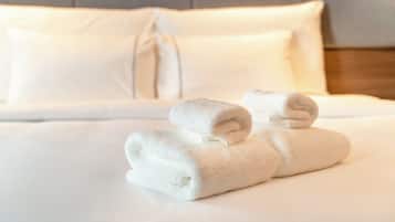 Una cama bien hecha con sábanas blancas y dos toallas enrolladas encima.