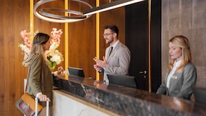 A reception desk with a marble top, wooden paneling on the walls, and a modern light fixture above.