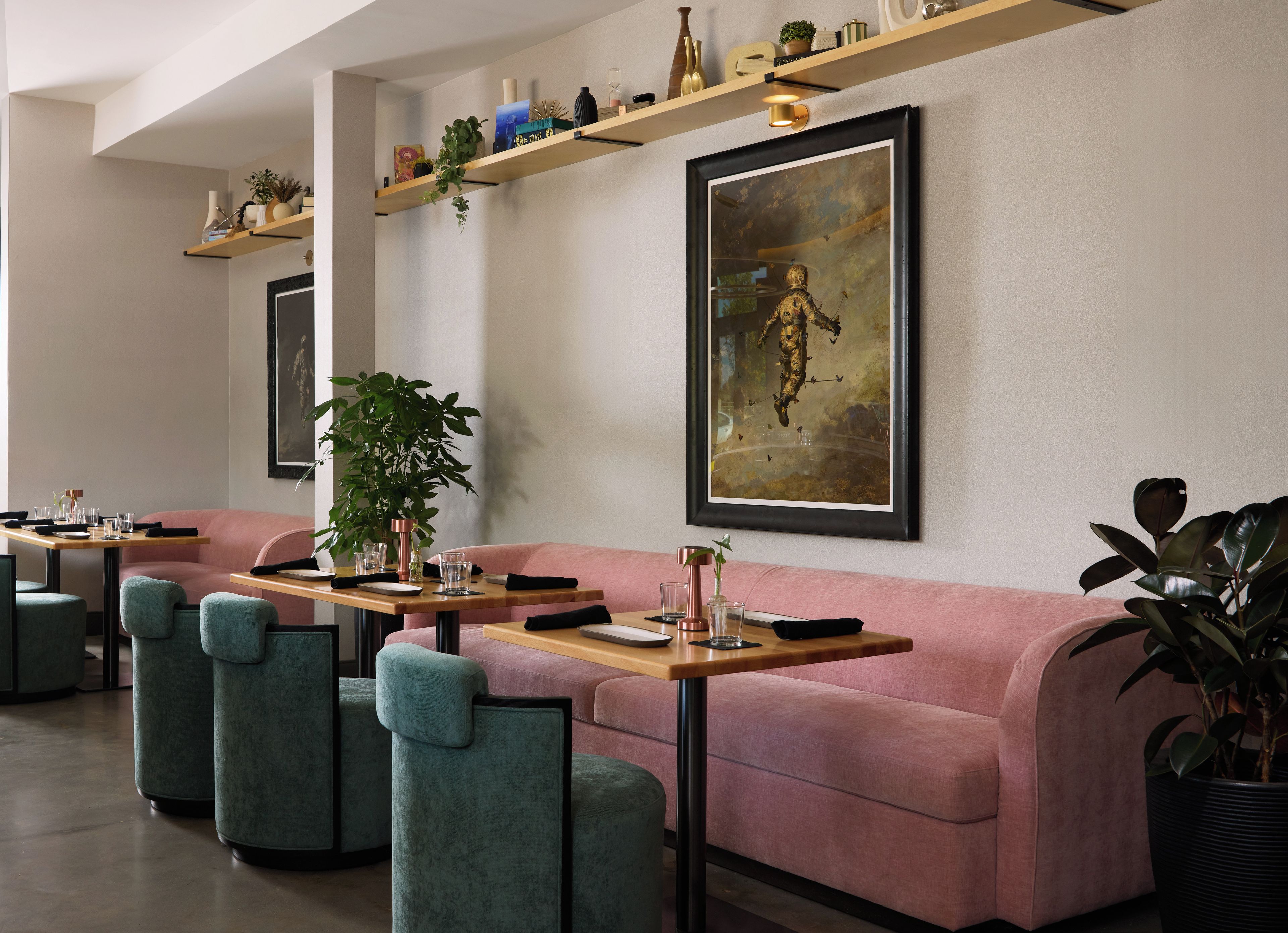 A modern restaurant with a pink sofa, teal chairs, and a wooden table set for dining.