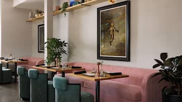 A modern restaurant with a pink sofa, teal chairs, and a wooden table set for dining.