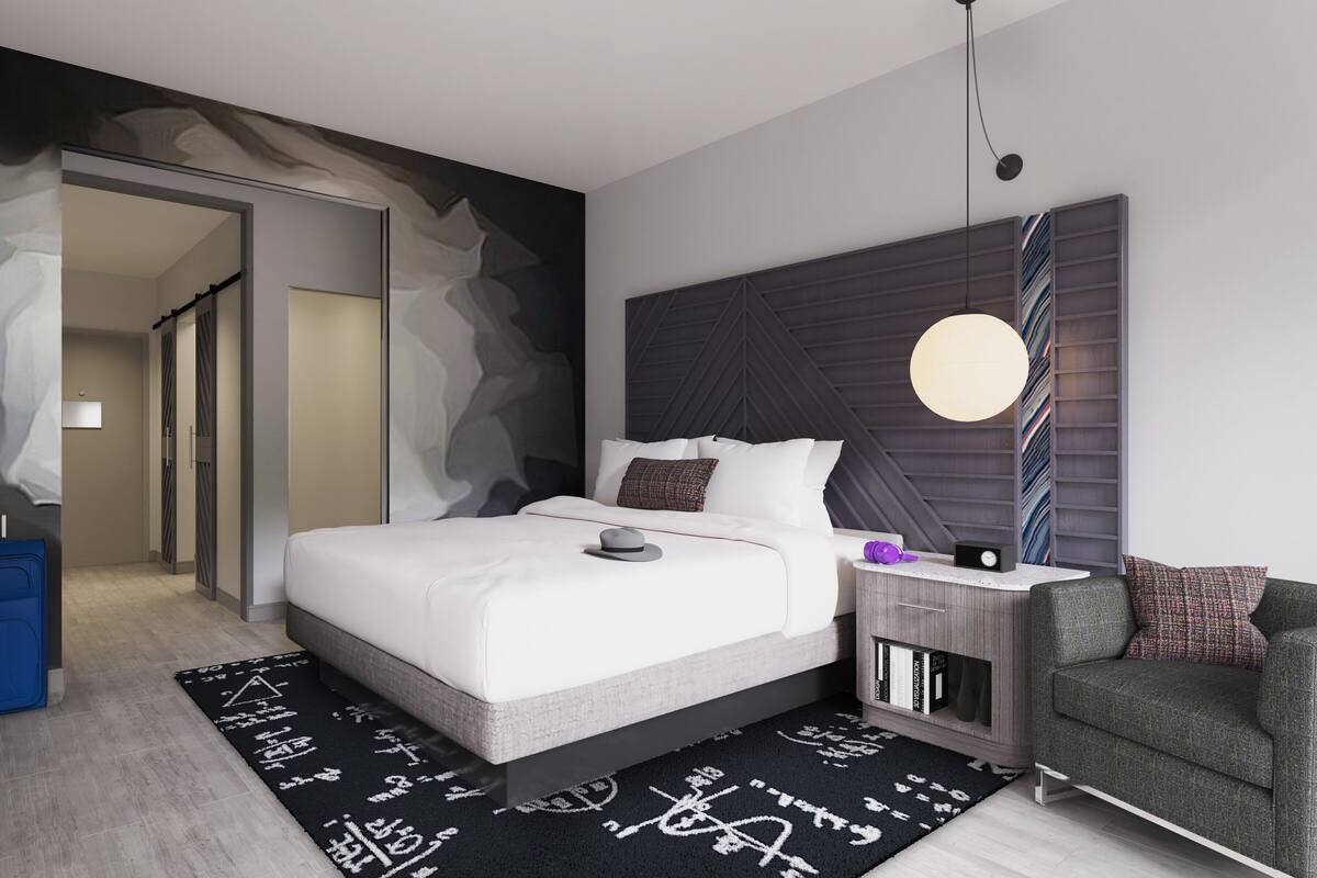Ein modernes Schlafzimmer mit einem großen Bett, einem Nachttisch mit Lampe, einem Sessel und einem Bücherregal.