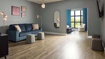 A modern living room with a blue sofa, ottomans, a large mirror, and a view through a window with blue curtains.