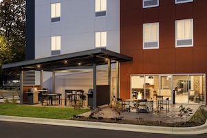 Un espacio de patio exterior con mesas, sillas, una parrilla y un hogar para fuego.