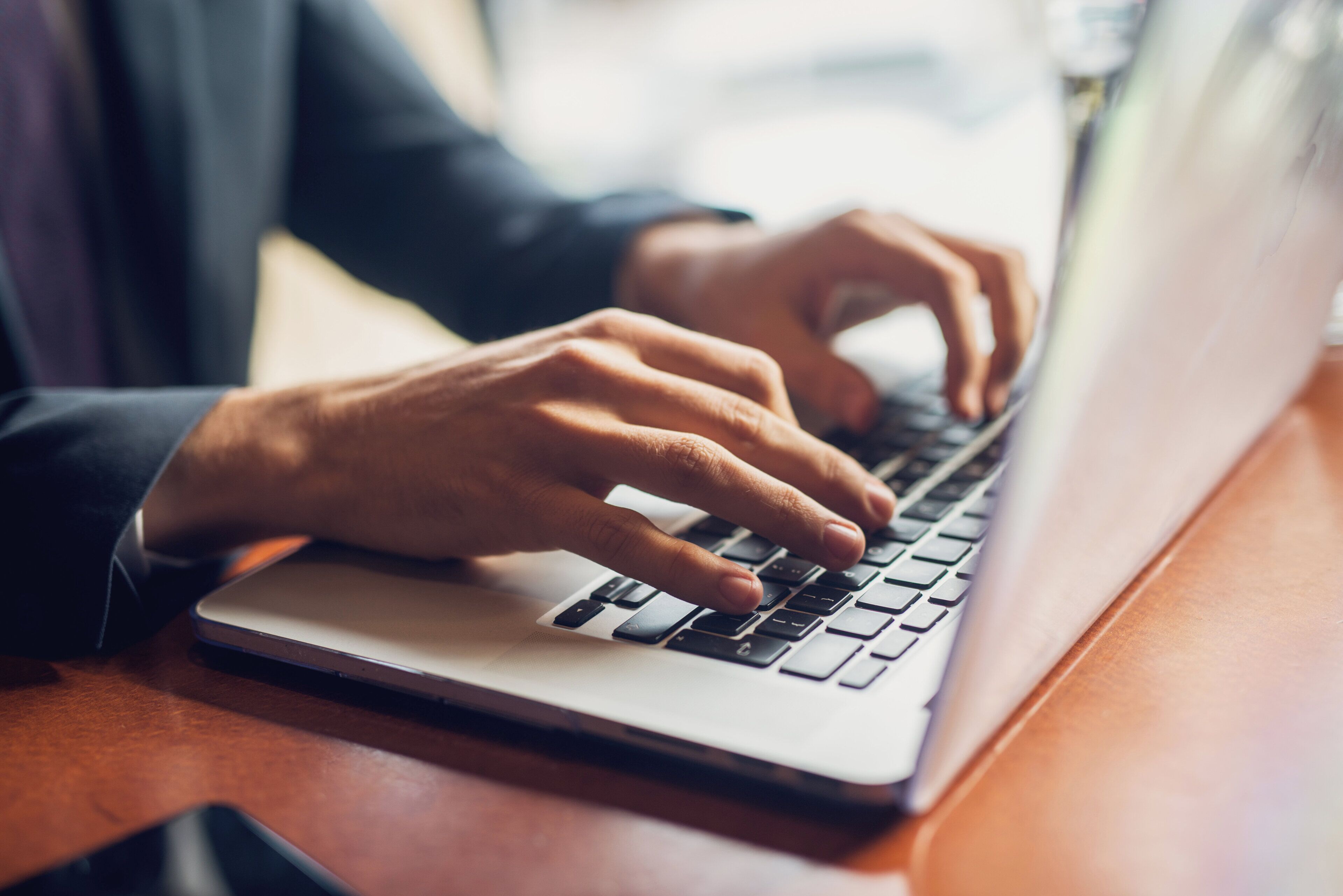 A person typing on a laptop placed on a wooden surface.