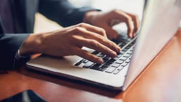 A person typing on a laptop placed on a wooden surface.