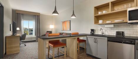 Una cocina moderna con una isla central, taburetes de bar, microondas y lavavajillas.