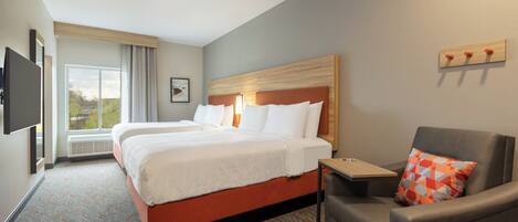 A hotel room with a large bed, a desk, a chair, and a TV mounted on the wall.