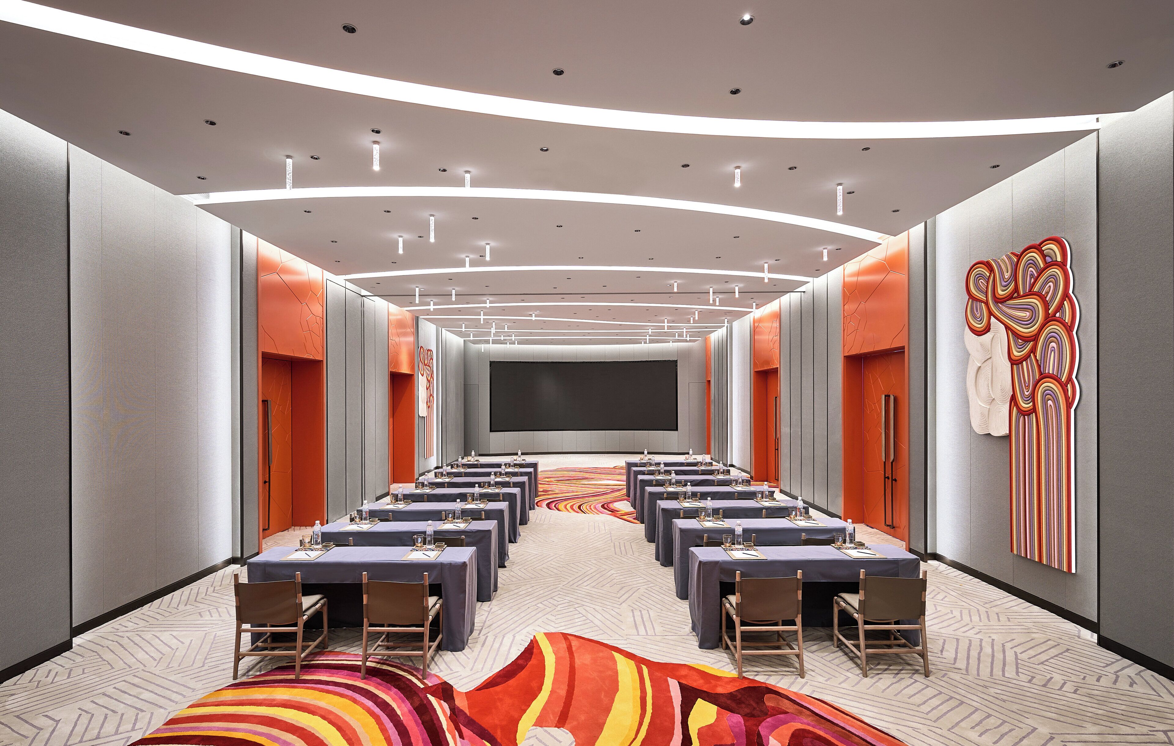 Une salle de conférence avec une longue table, des chaises, un grand écran et une moquette colorée.