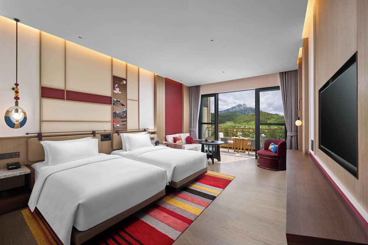 Une chambre d’hôtel avec deux lits, une télévision, un balcon avec vue sur la montagne et un coin repas.