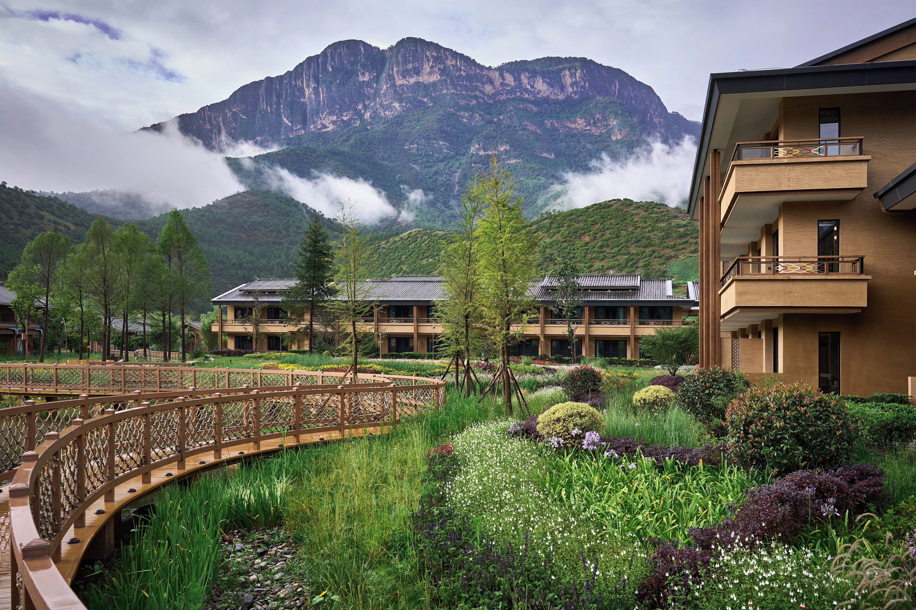 A hotel with a traditional roof, surrounded by lush gardens and a wooden bridge.