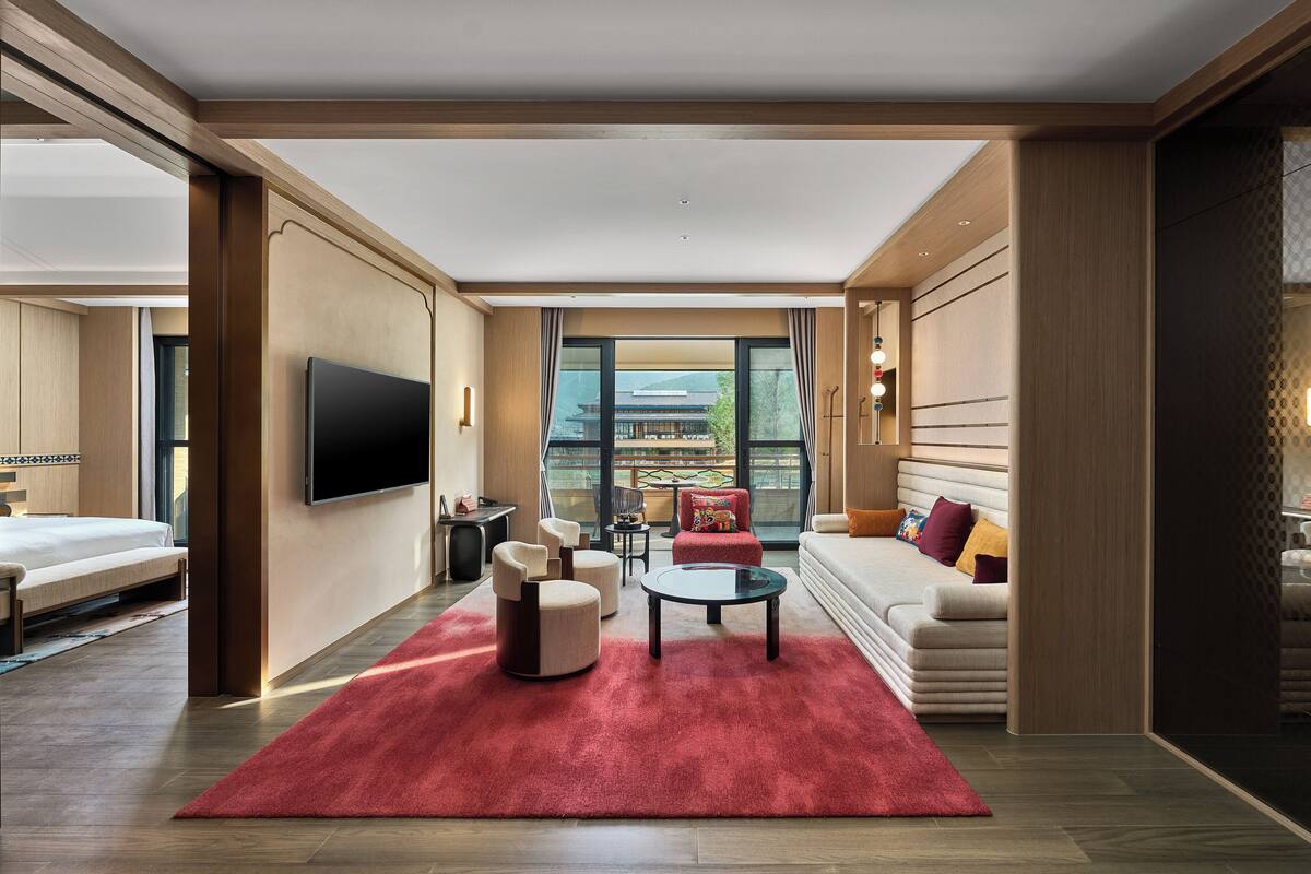 Ein modernes Hotelzimmer mit großem Fenster, einem Flachbildfernseher, einer Couch, einem Couchtisch und einem roten Teppich.
