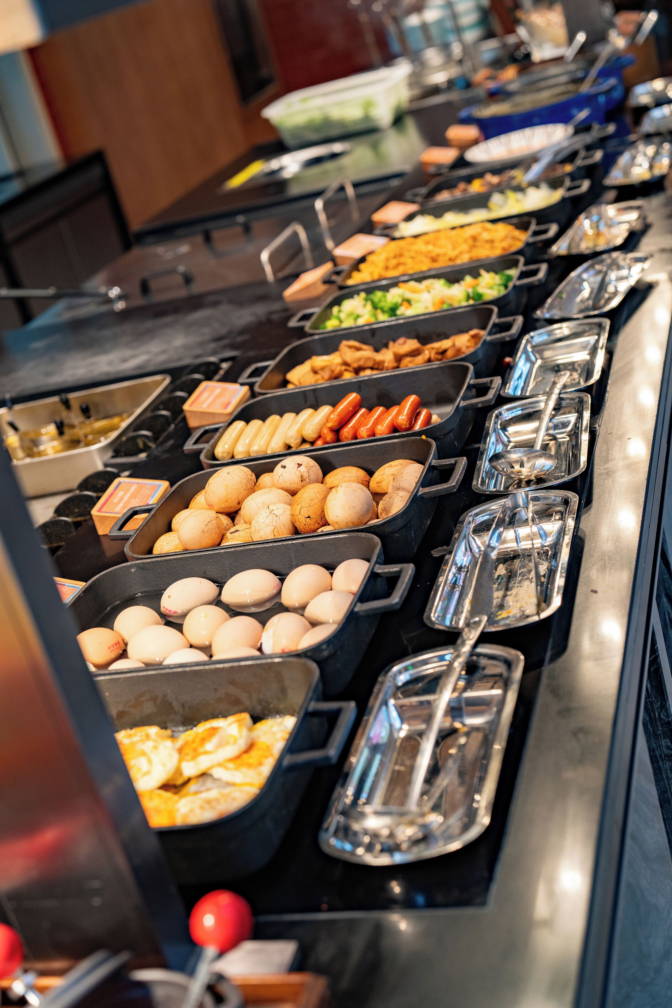 A buffet with various food items including eggs, sausages, and vegetables.