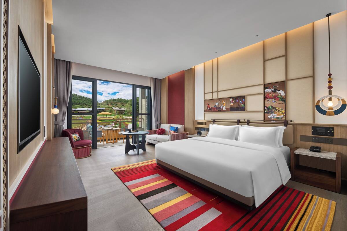Une chambre d’hôtel moderne, dotée d’un grand lit, d’un bureau, d’une chaise et offrant une vue sur l’extérieur.
