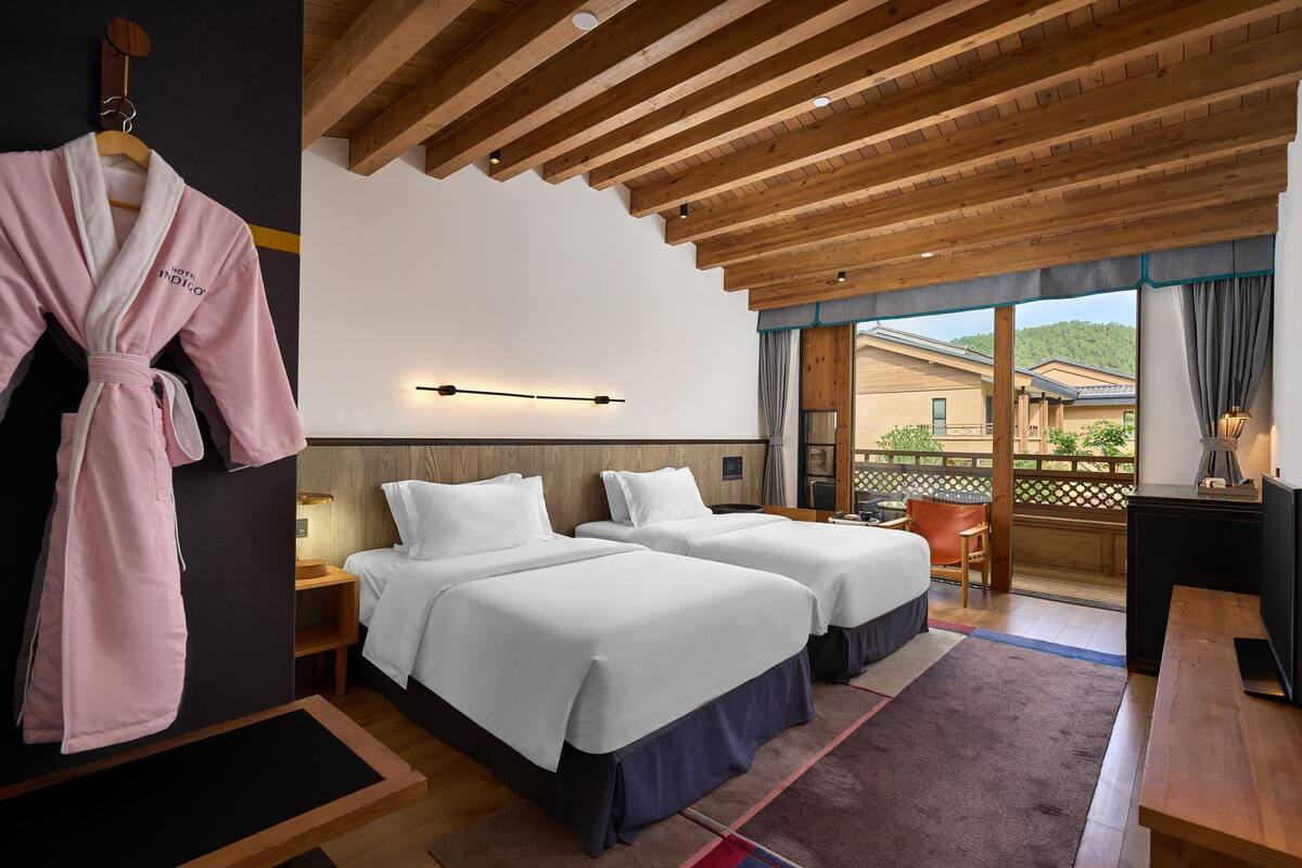 Une chambre d’hôtel avec deux lits, un plafond en bois, un bureau et une vue sur l’extérieur.