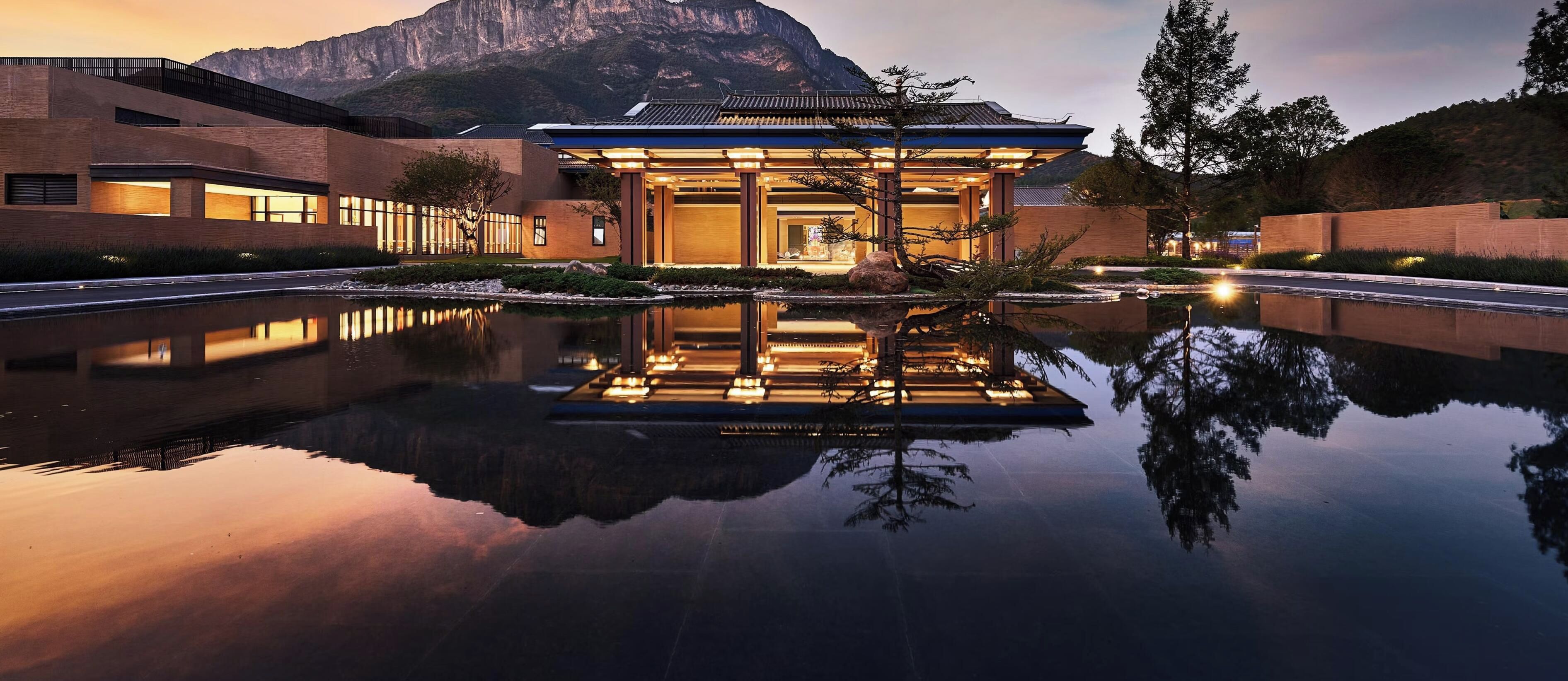 Ein modernes Gebäude mit einem spiegelnden Pool, einem Berg im Hintergrund und traditionellen architektonischen Elementen.