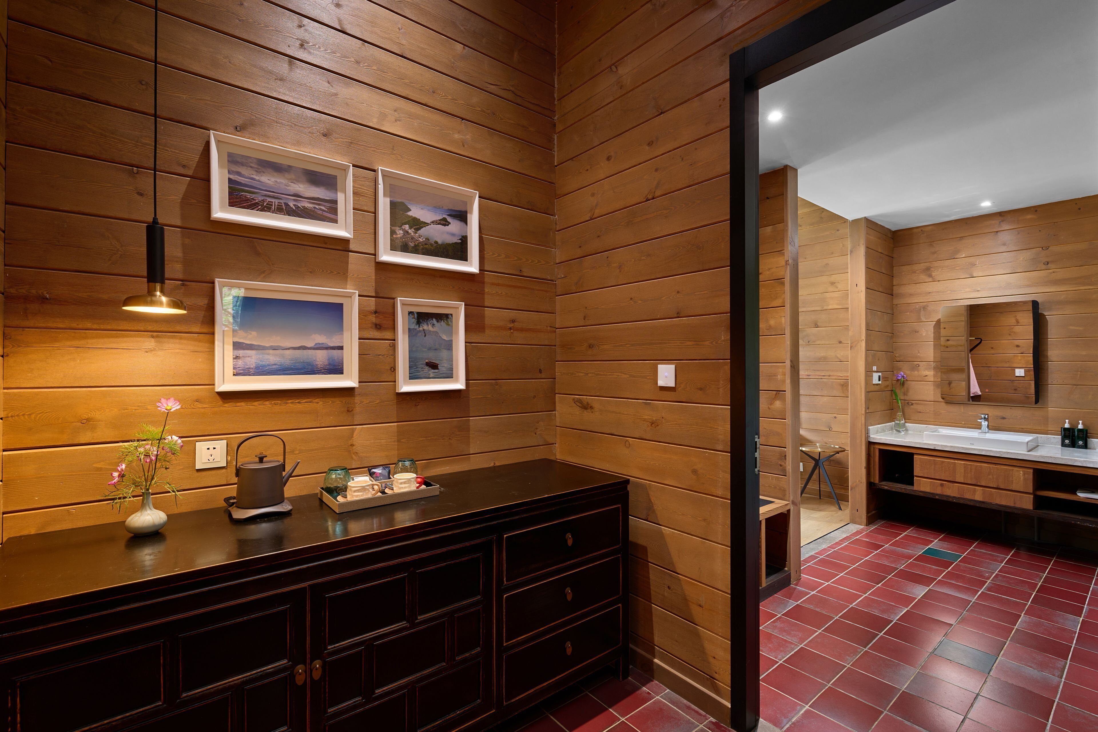 A wooden-paneled bathroom with a vanity, framed pictures, and a red-tiled floor.
