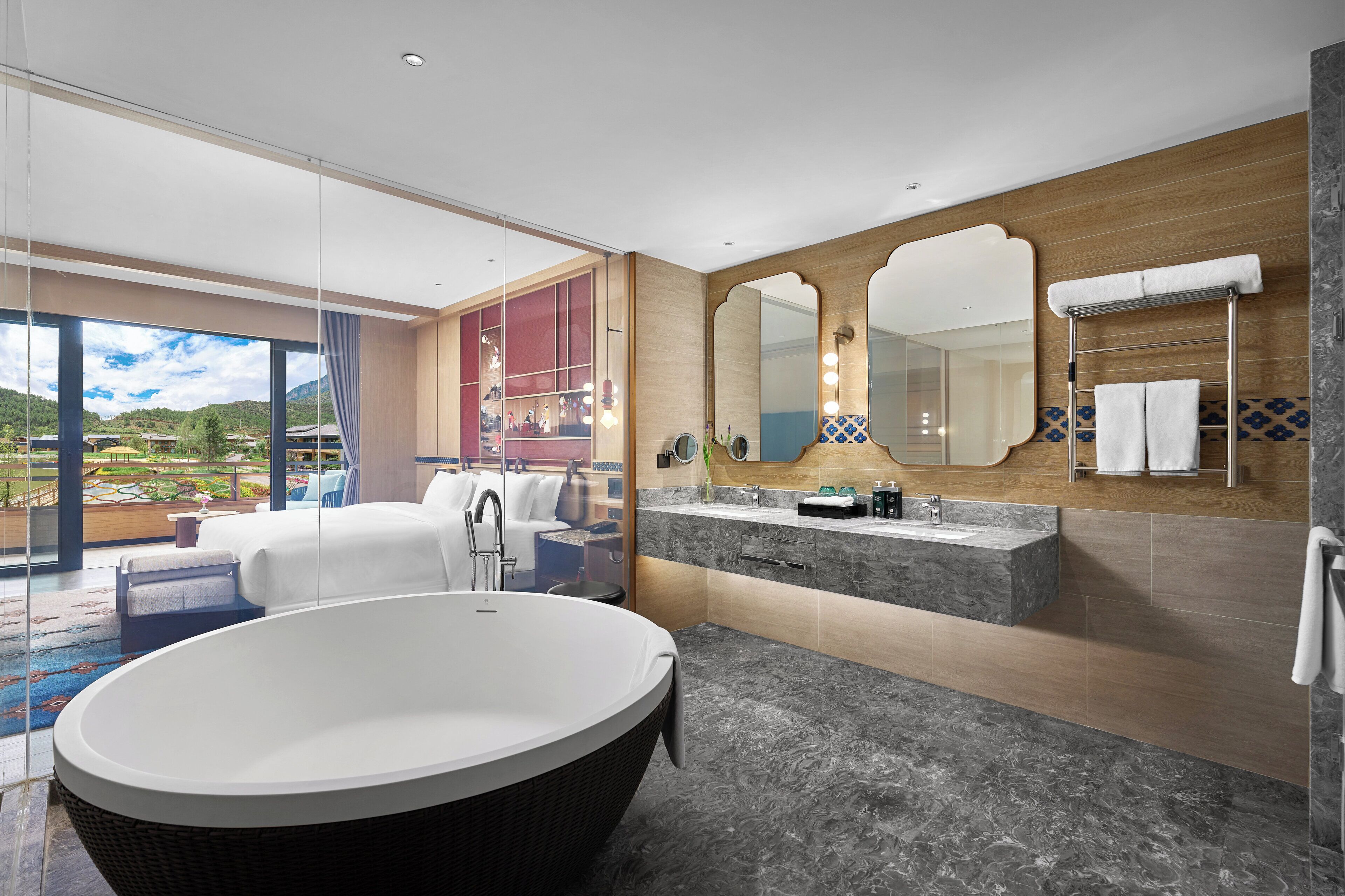 A modern bathroom with a large freestanding bathtub, a vanity with a mirror, and a view of a landscaped area through a glass door.