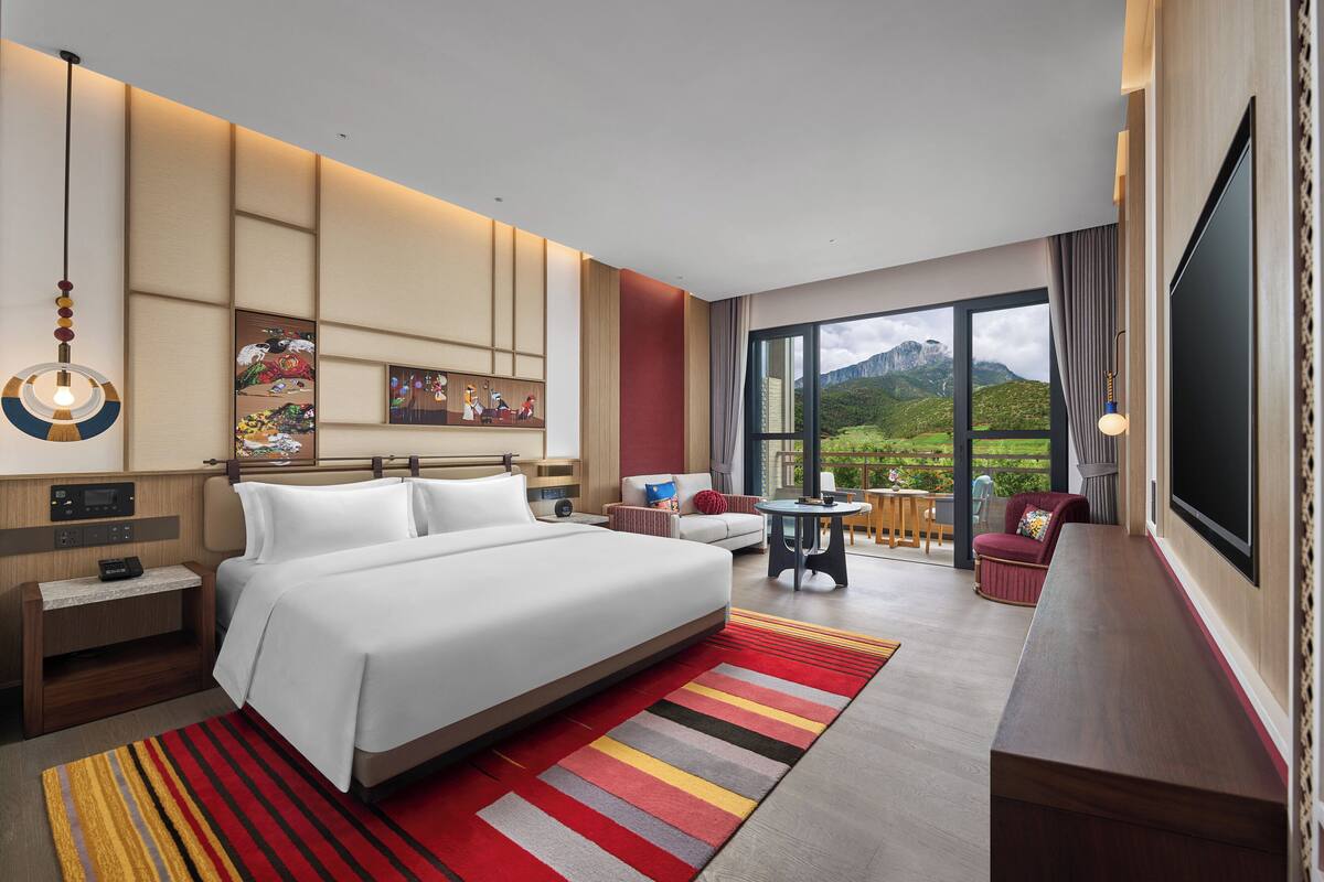 Une chambre d’hôtel dotée d’un grand lit, d’un bureau, d’une chaise, d’une télévision et d’un balcon offrant une vue sur la montagne.