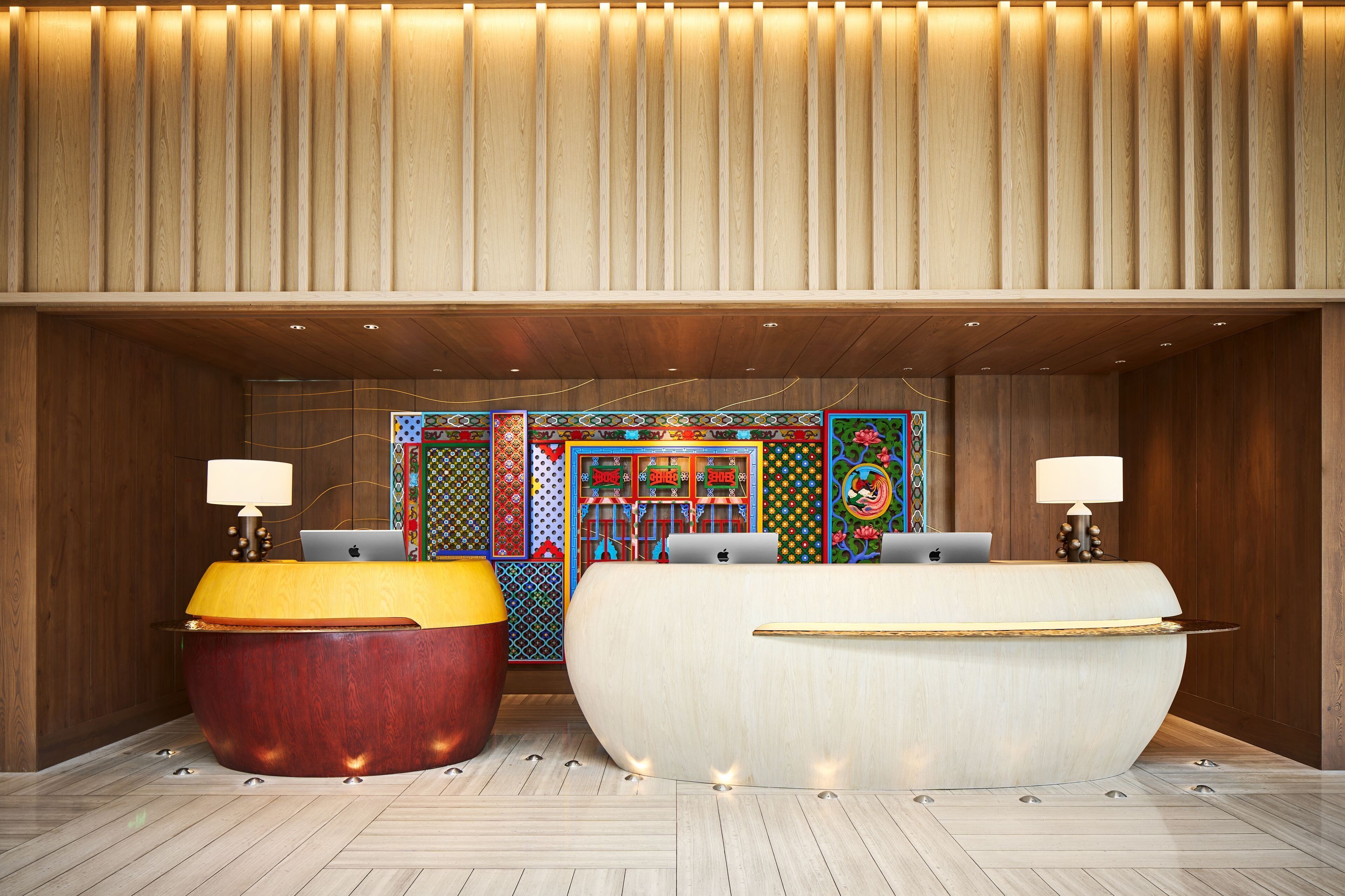 A modern reception area with two large, curved reception desks, a wooden panel wall, and colorful artwork on the back wall.