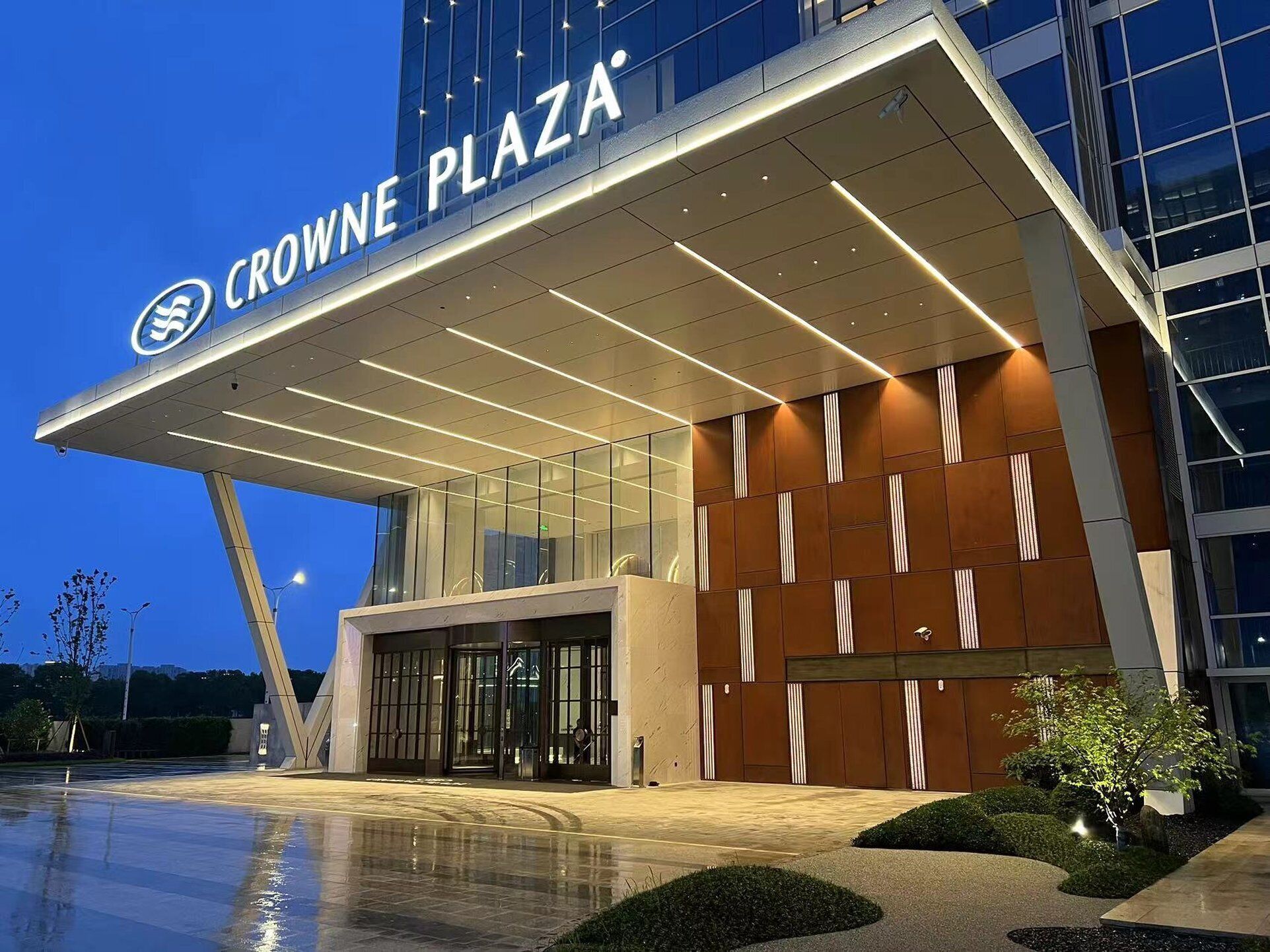 Une entrée d'hôtel moderne avec une façade en verre, une enseigne bien visible indiquant « CROWNE PLAZA » et un espace d'entrée bien éclairé.