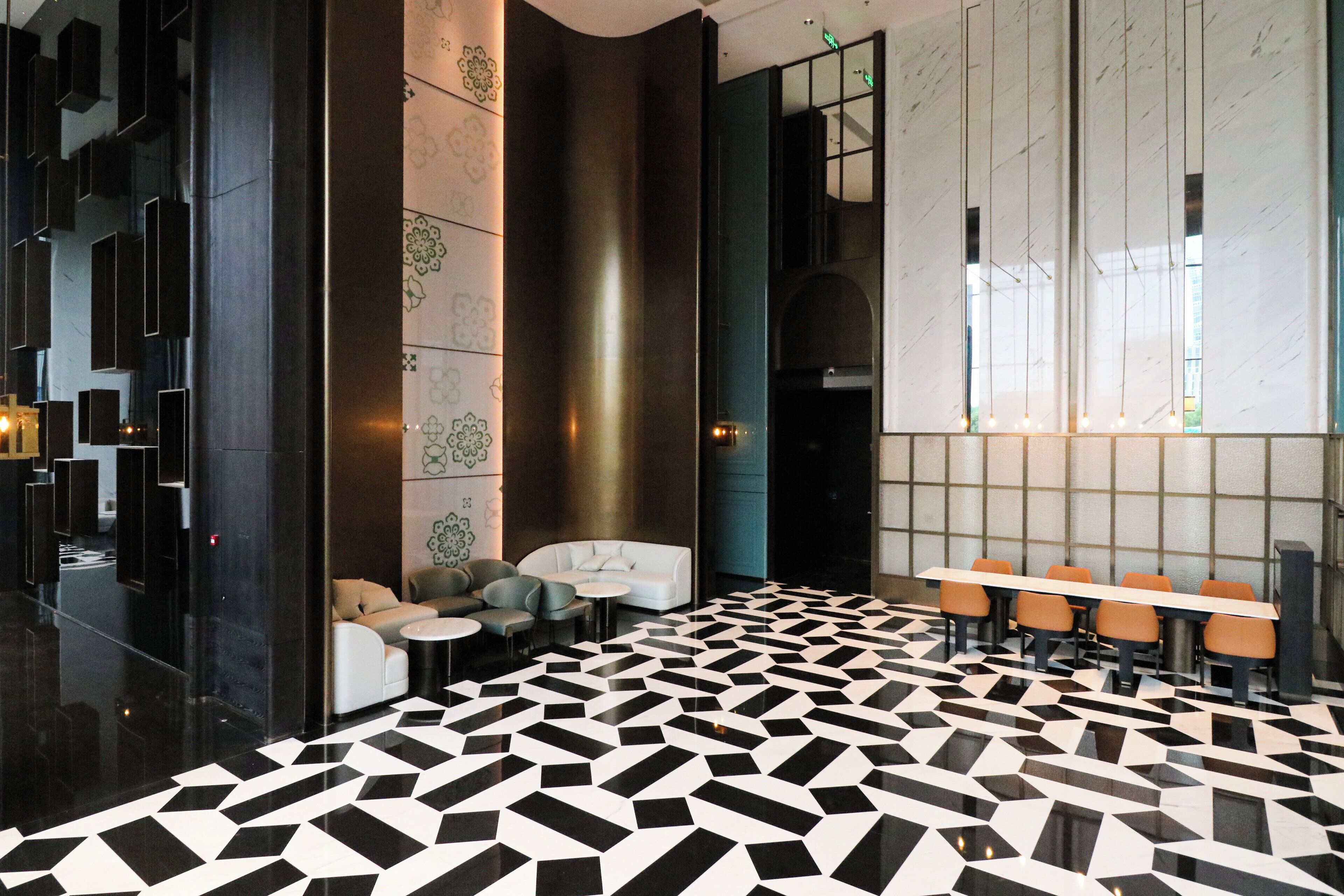 A modern lobby with a geometric black and white floor pattern, seating areas, and a large window with natural light.