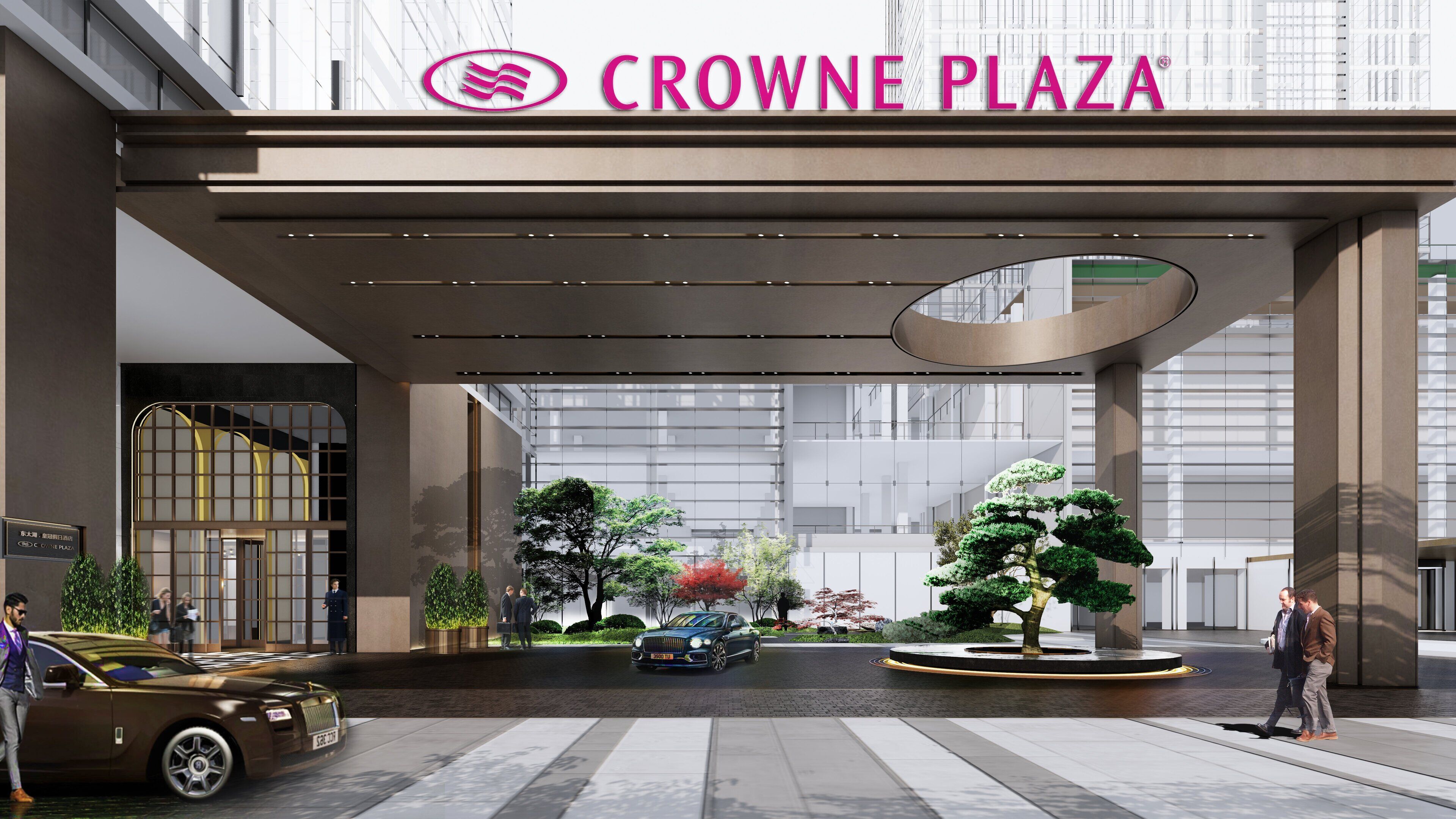 A modern hotel entrance with a glass facade, a prominent sign reading "CROWNE PLAZA," and a landscaped area with trees and a car.