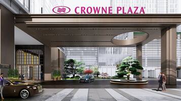 A modern hotel entrance with a glass facade, a prominent sign reading "CROWNE PLAZA," and a landscaped area with trees and a car.