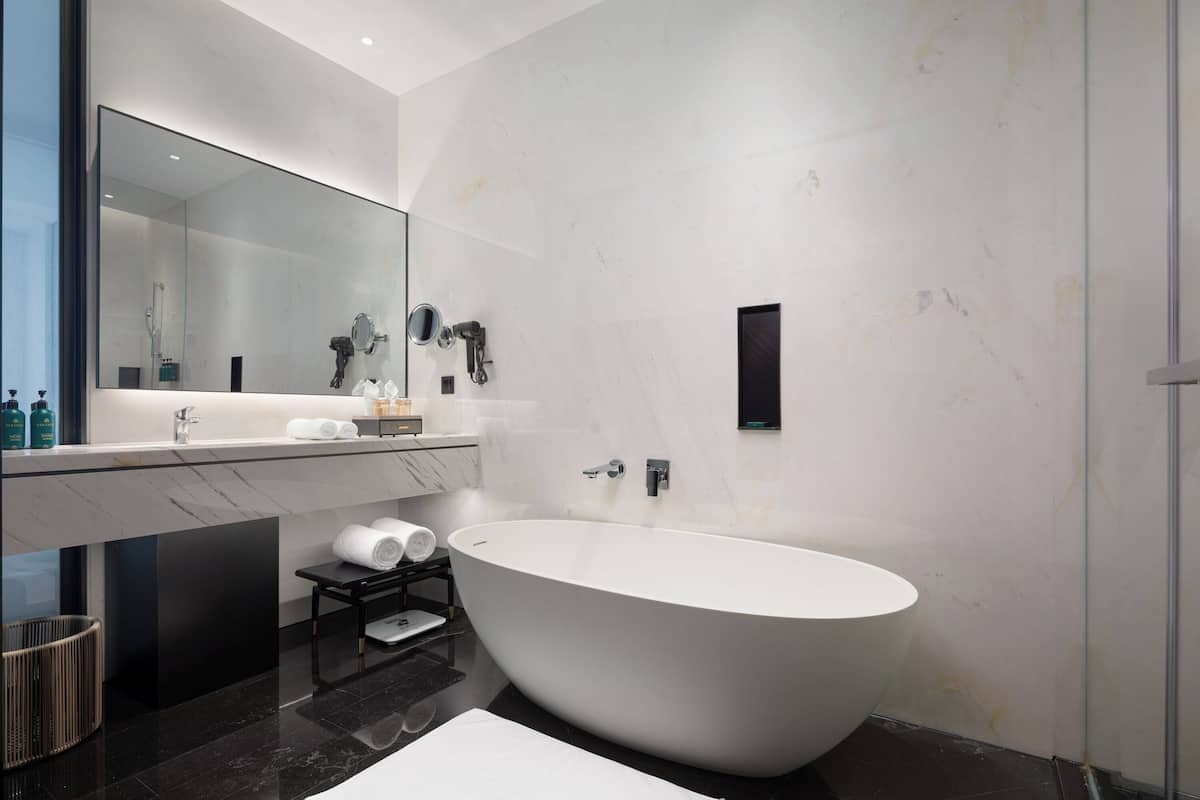 A modern bathroom with a freestanding bathtub, a large mirror, and a marble countertop.