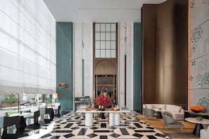 A modern hotel lobby with a geometric black and white floor pattern, a central buffet table, and a seating area with sofas and chairs.
