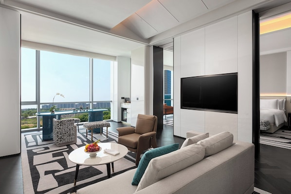 Habitación de hotel moderna con una televisión grande, un sofá, una mesa de centro y un balcón con vistas a la ciudad.