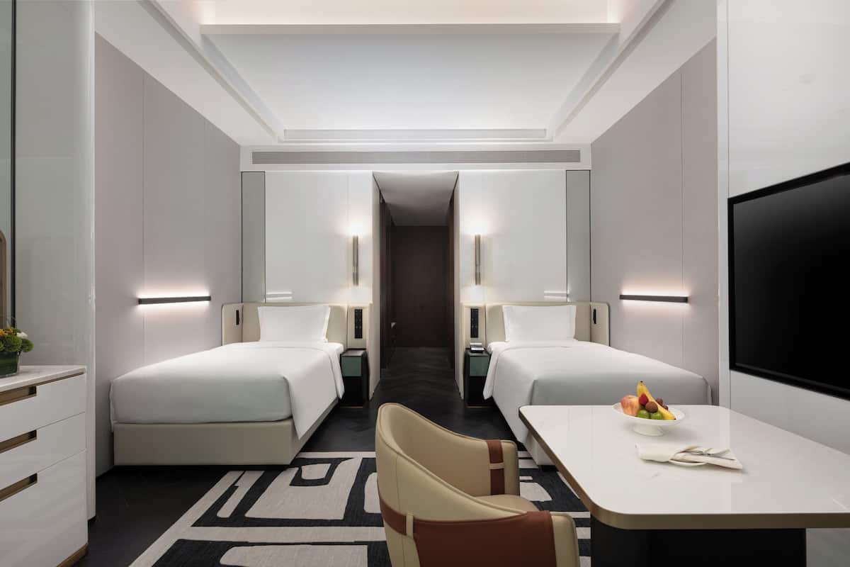 A hotel room with two beds, a desk with a fruit bowl, and a TV.