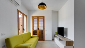 Uma sala de estar moderna com um sofá verde, uma TV em um console de madeira e uma luminária pendente.