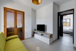 A modern living room with a green sofa, a TV on a wooden stand, and a sliding door leading to a balcony. - Lemon Apartment 1 - Dreaming Vacation (Tortolì)