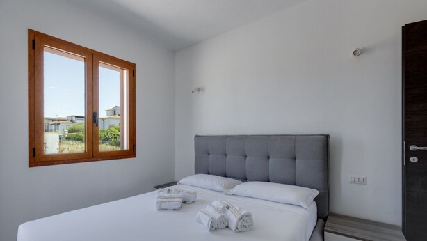 Quarto com uma cama grande, janela de madeira e guarda-roupa escuro.