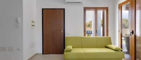 Ein modernes Wohnzimmer mit einem grünen Sofa, einer Holztür und einem großen Fenster.