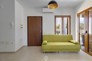 Un salon moderne avec un canapé vert, une porte en bois et une grande fenêtre.