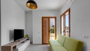 Una sala de estar moderna con un televisor de pantalla plana sobre una consola de madera, un sofá verde y un puerta corrediza de vidrio que da a un área exterior.