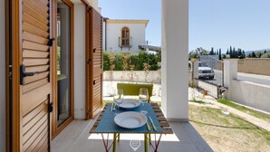 Un espacio exterior con comedor, una mesa lista para dos personas, una puerta de madera y una vista de un edificio al fondo.