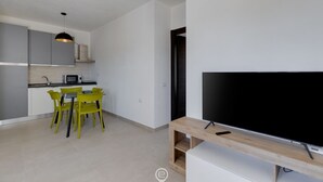 Un espacio de estar moderno con comedor, cocina y un televisor de pantalla plana grande.
