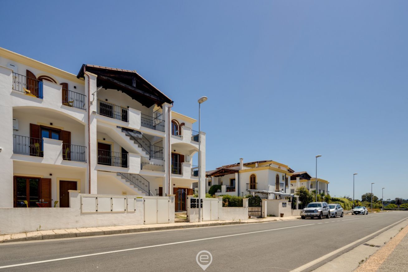 Un immeuble résidentiel à plusieurs étages, doté de balcons, d’une entrée sécurisée et situé dans une rue où les voitures sont garées.