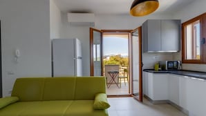 A modern kitchen with a built-in oven, a dining area with a table and chairs, and a green sofa. - Orange Apartment 4 - Wonderful Vacation (Tortolì)