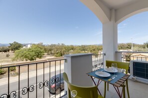 A balcony with a table set for two, a car parked on the street, and a clear view of the surrounding landscape.