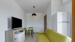 A modern living room with a flat-screen TV, a sofa, a dining table with chairs, and a white refrigerator. - Orange Apartment 4 - Wonderful Vacation (Tortolì)