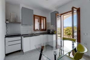 A modern kitchen with white cabinets, a glass table, and a view of the outdoors.
