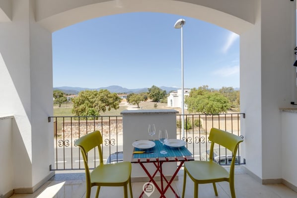 A balcony with a table set for two, a street view, and a clear sky.