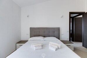 A modern bedroom with a large bed, two bedside tables, and a wardrobe.
