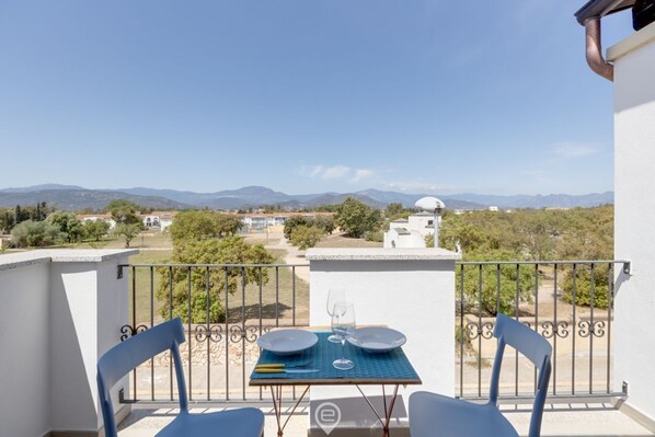 A balcony with a table set for two, overlooking a mountainous landscape.