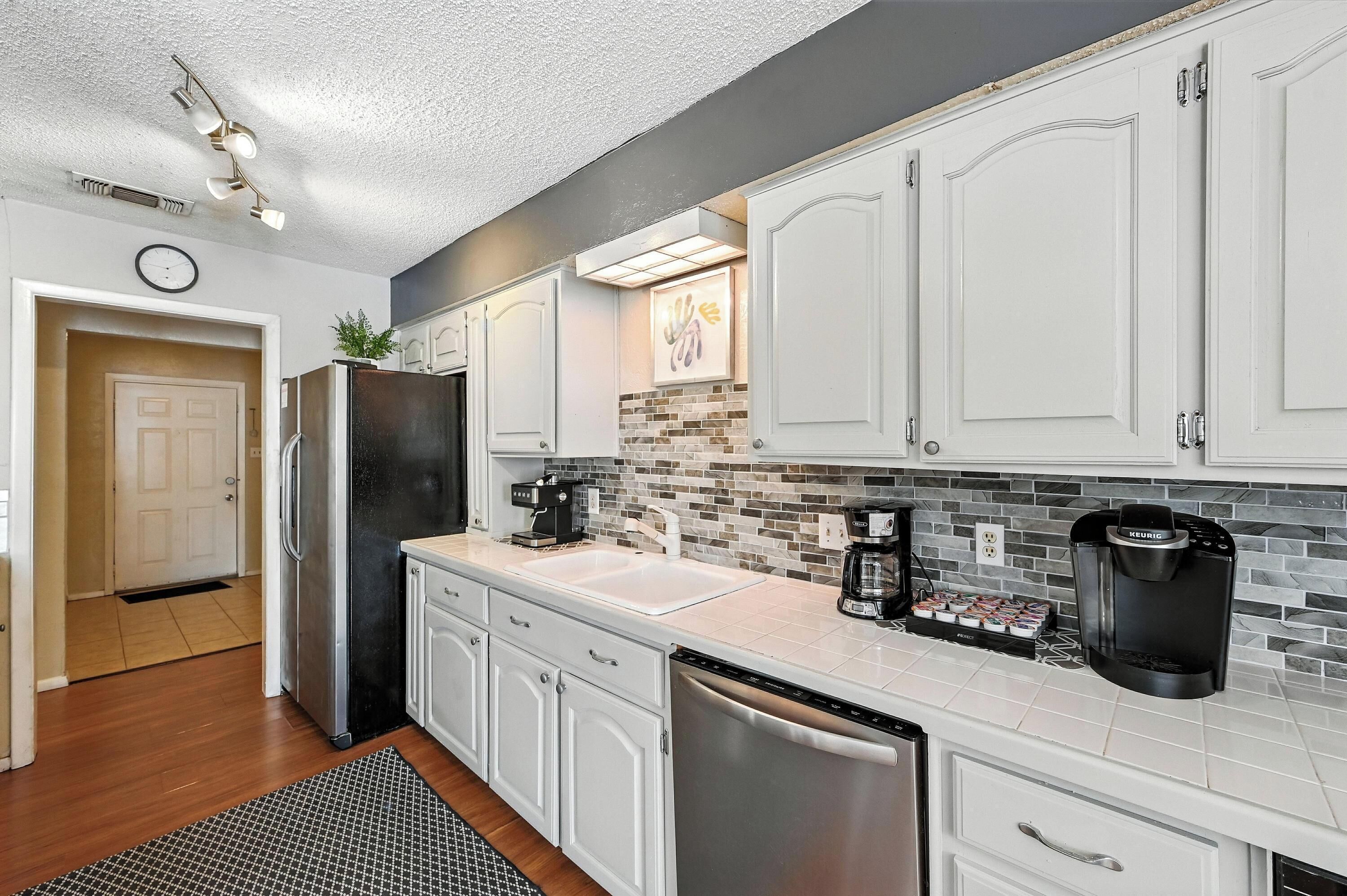 A modern kitchen with white cabinetry, a black refrigerator, a coffee maker, and a dishwasher.