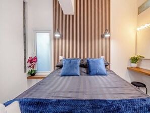 Una camera da letto moderna con un letto, due lampade da comodino, una finestra, una pianta in vaso e uno specchio con luci.